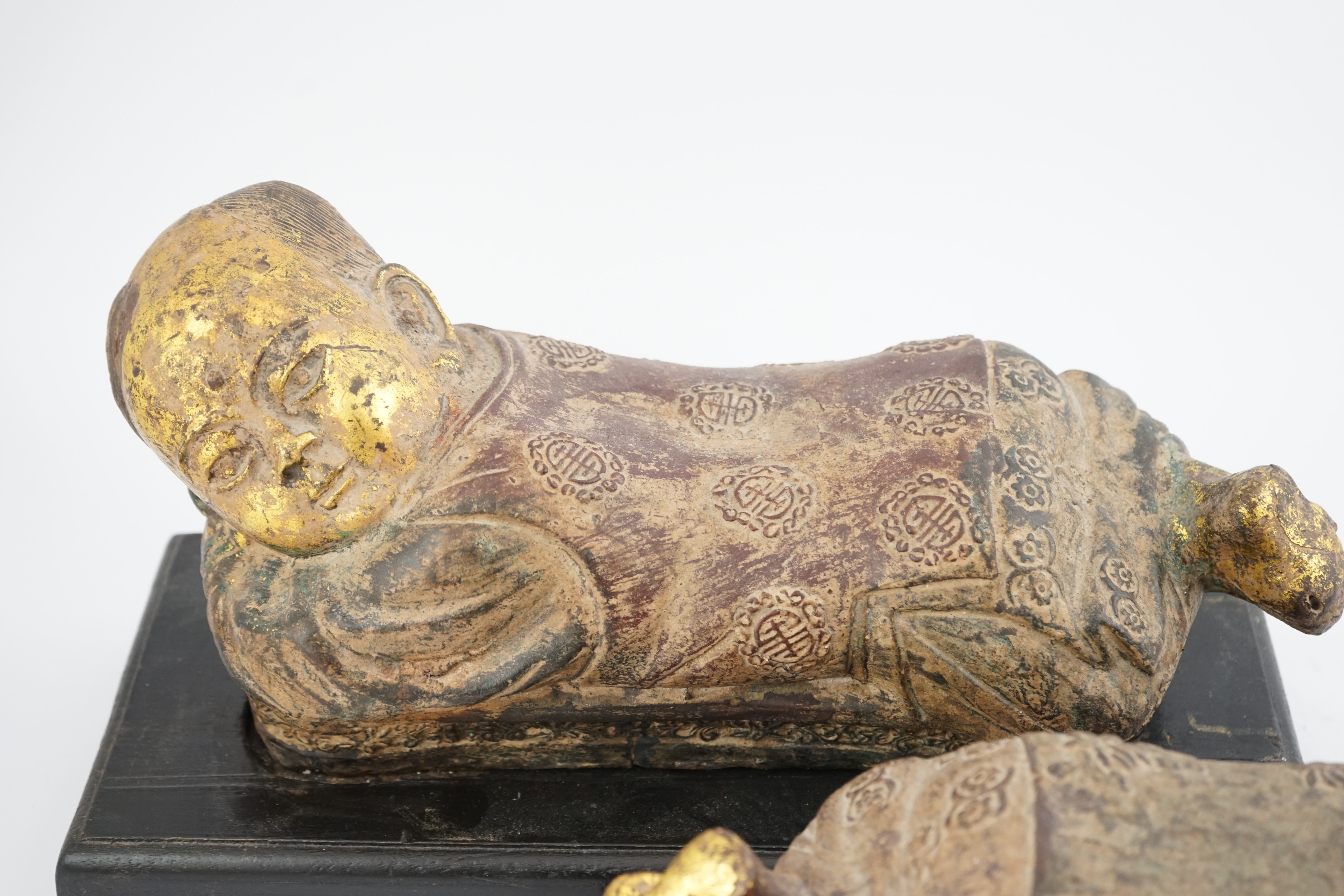 Two Chinese polychrome decorated iron pillows, modelled as sleeping children, on ebonised wood plinths, 44cm long. Condition - fair to good